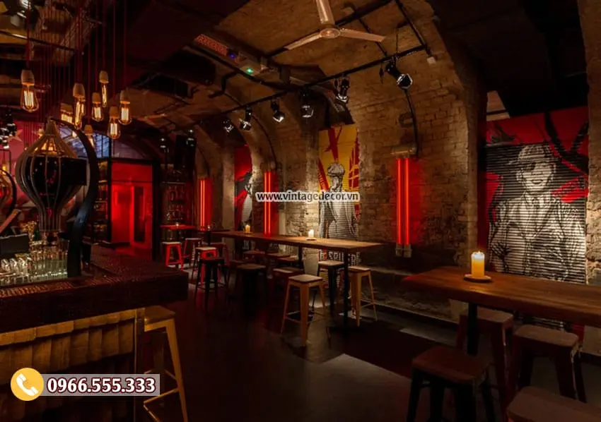 Khu bàn đứng mặt gỗ trong hầm vòm gạch, tranh tường lớn vẽ người và nền đỏ, đèn rọi ray trên trần