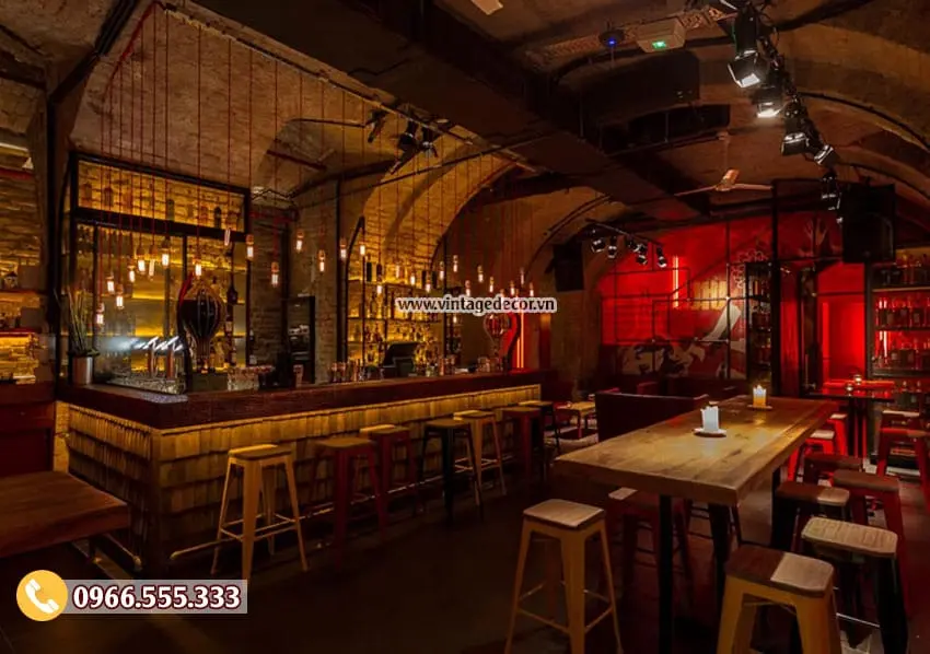 Quầy bar dài ốp gỗ sáng đèn dưới mặt quầy, ghế cao vàng và đỏ, bàn gỗ cao có nến, trần vòm gạch