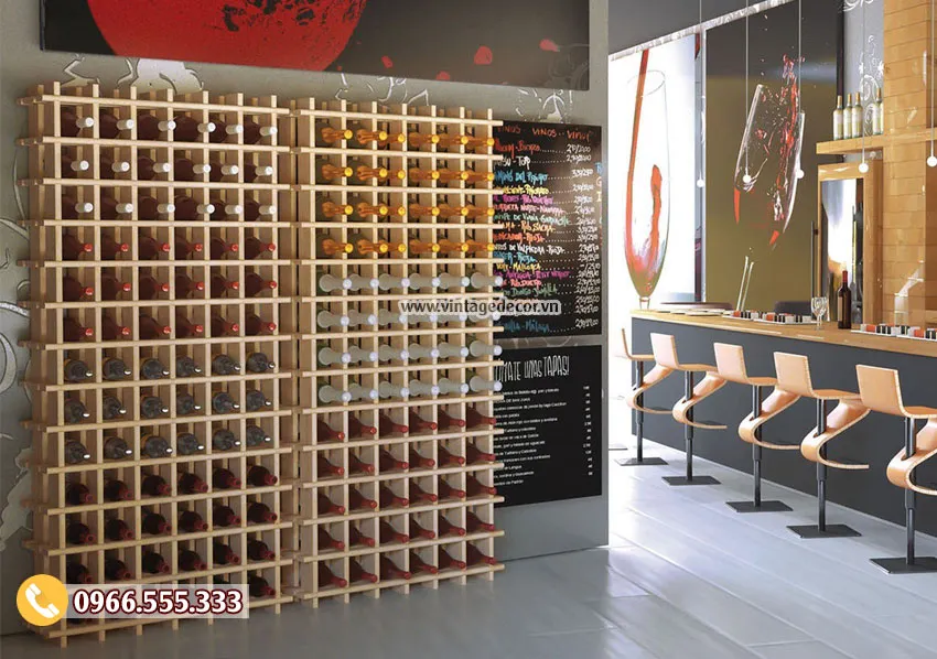 Kệ lưới ô gỗ sáng màu cao kín tường, mỗi ô một chai nằm, bên phải là quầy bar có ghế cao