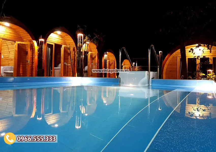 Cụm bungalow mái vòm NB20 ban đêm, đèn vàng hắt sáng mặt tiền gỗ, hồ bơi phản chiếu ánh đèn