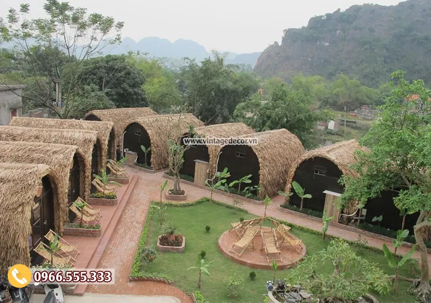 Toàn cảnh cụm bungalow mái vòm phủ lá NB28 quanh vườn cỏ, lối gạch đỏ, phía xa là núi đá