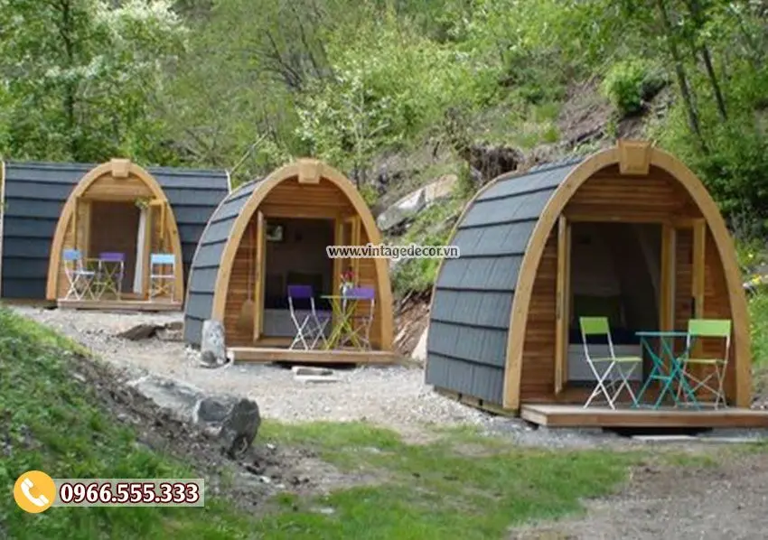 Ba căn bungalow mái vòm lợp tấm màu xám xếp hàng trên sườn đồi, mỗi căn có hiên gỗ và bàn ghế