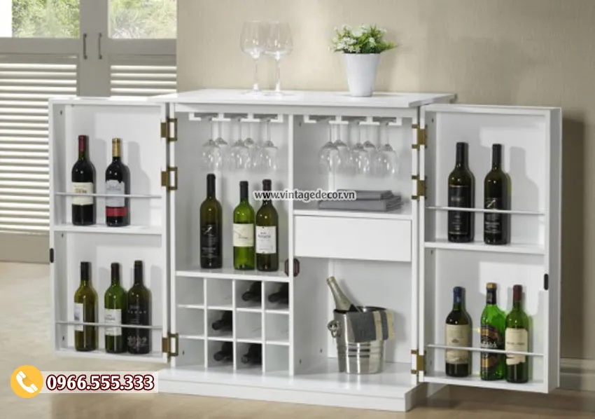 Tủ bar sơn trắng mở hai cánh, mỗi cánh có thanh chặn chai, giữa treo ly chân cao