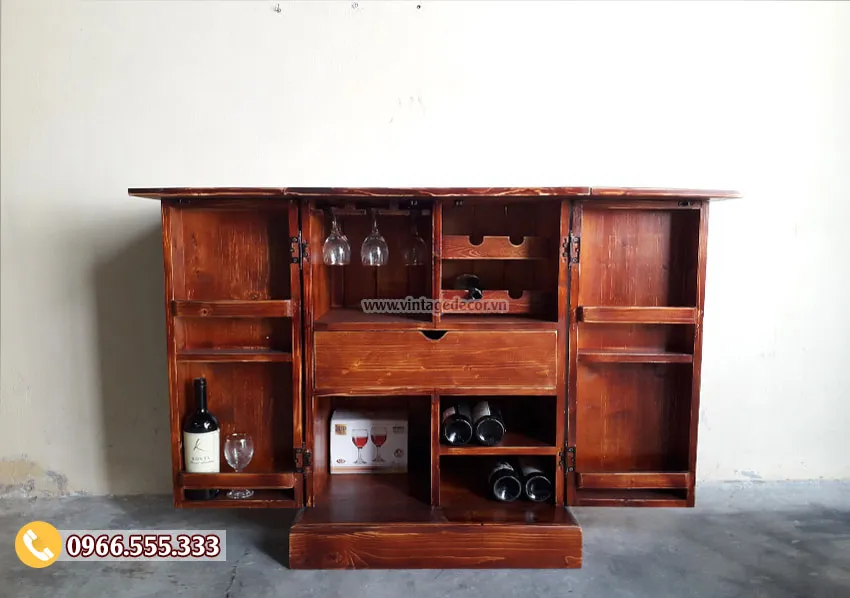 Tủ rượu gỗ nâu đỏ đang mở hết các cánh, giữa là ô để chai, treo ly phía trên, ngăn kéo ở giữa