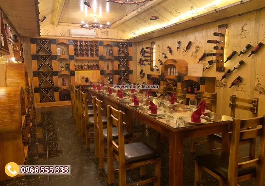 Phòng ăn dài tường ốp gỗ sáng, chai rượu cắm nghiêng trên tường, ô trám chai dọc phòng, bàn dài giữa