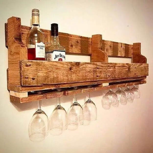 Kệ gỗ thô kiểu pallet treo tường, trên đặt chai whisky, phía dưới treo một hàng ly vang