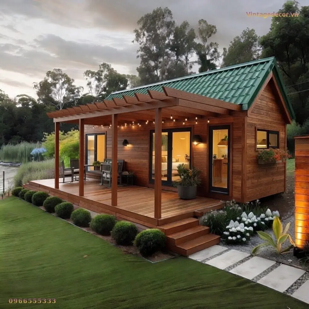 Nhà gỗ homestay S9 mái ngói xanh lúc chiều tối, hiên gỗ dưới giàn pergola giăng đèn, cửa kính sáng đèn