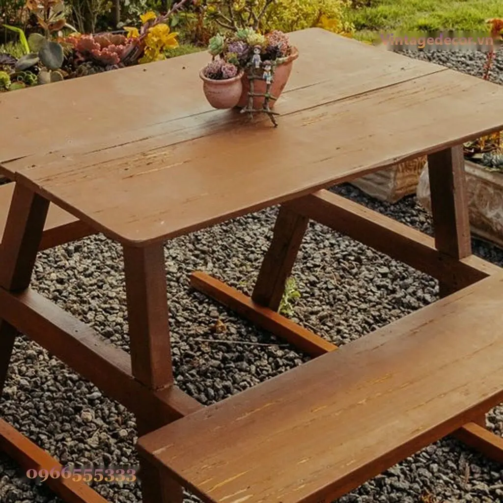 Cận cảnh bộ picnic BG12: mặt bàn ván rộng, chân choãi chữ A và thanh ngang thấp đỡ ghế băng, nền sỏi đen